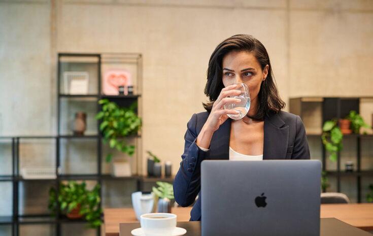 Kollegin trinkt Wasser vor ihrem PC
