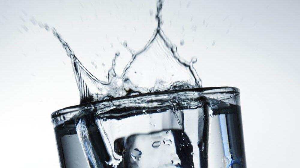 großer Eiswürfel fällt in Wasserglas