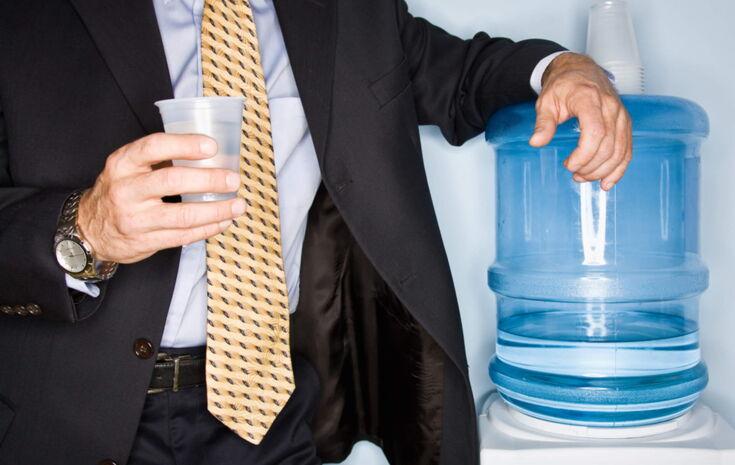 Ein Geschäftsmann mit gelber Krawatte steht an einem Wasserspender