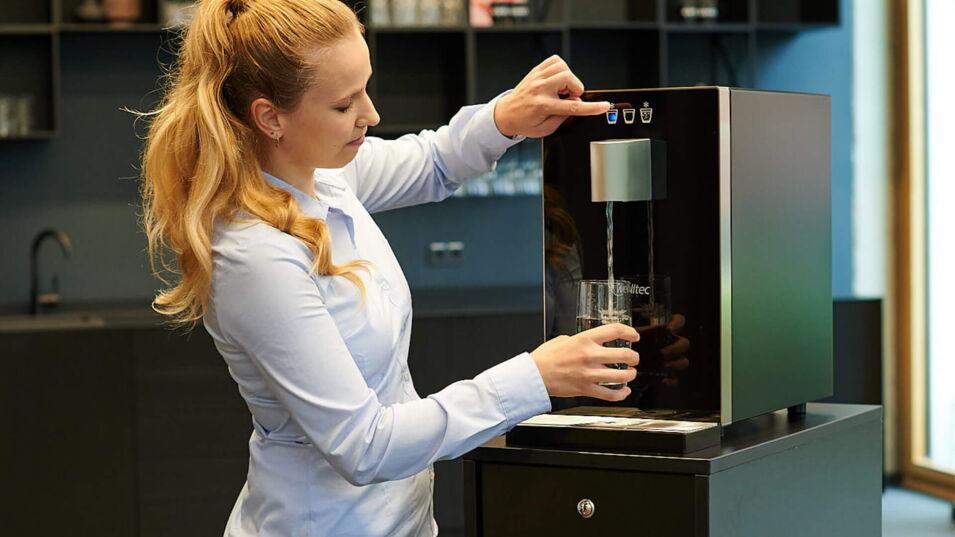 Eine Frau füllt Wasser in ein Glas an einem Wasserspender