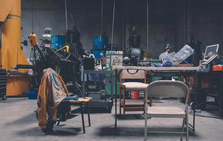 Fabrikhalle mit Tisch, Stuehlen und Maschinen im Hintergrund
