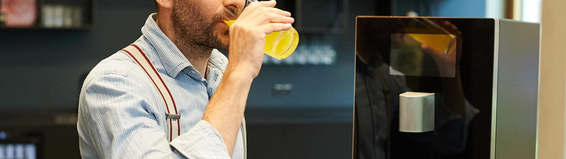 Mann trinkt abgefüllte Fruchtschorle am Wasserspender im Büro