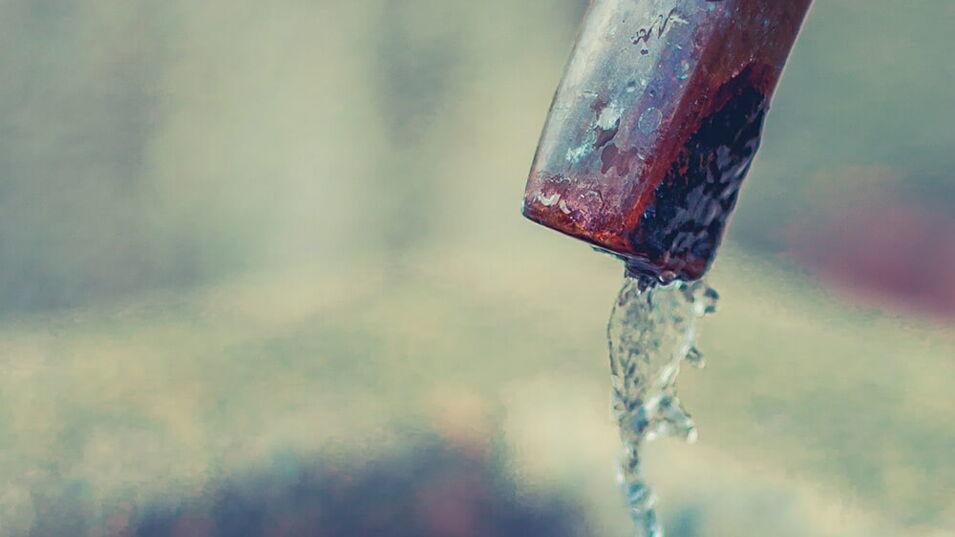 Wasser tropft aus einem Hahn in einen Brunnen