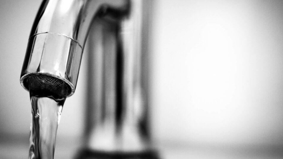 Schwarz-Weiss-Fotografie eines Edelstahlwasserhahns mit Wasserstrahl