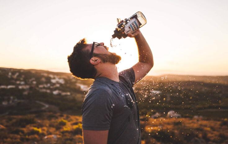 Mann trinkt Wasser aus Flasche in Natur