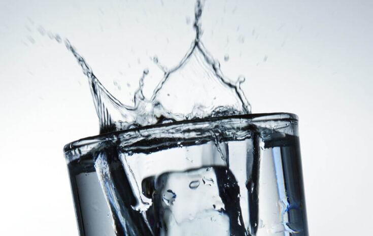 großer Eiswürfel fällt in Wasserglas