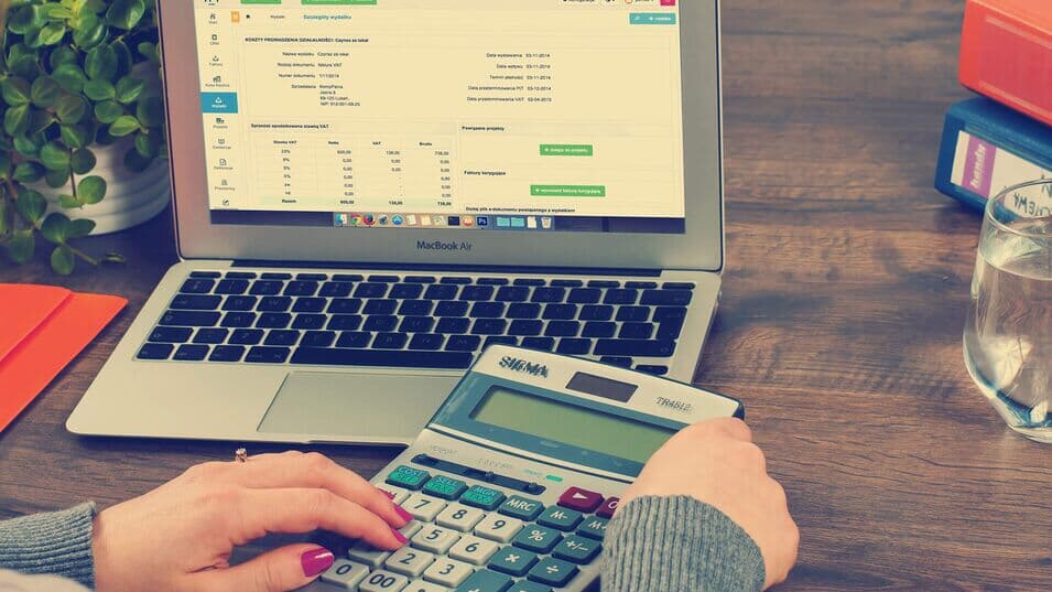 Frau an Schreibtisch mit Laptop und Taschenrechner