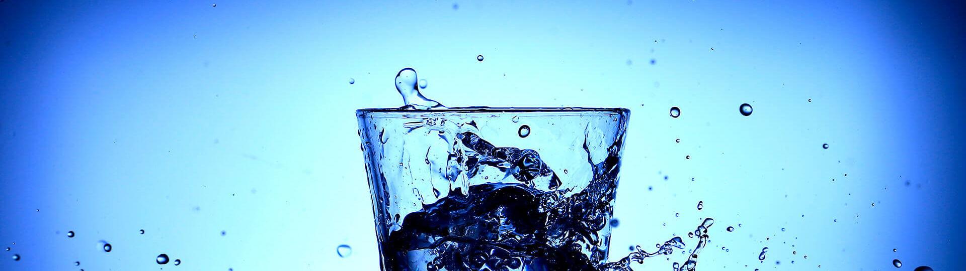 Spritzendes Wasser und ein Wasserglas vor blauem Hintergrund