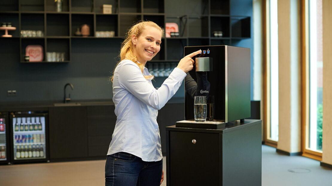 Junge Frau zieht sich ein Glas Wasser aus dem Wasserspender