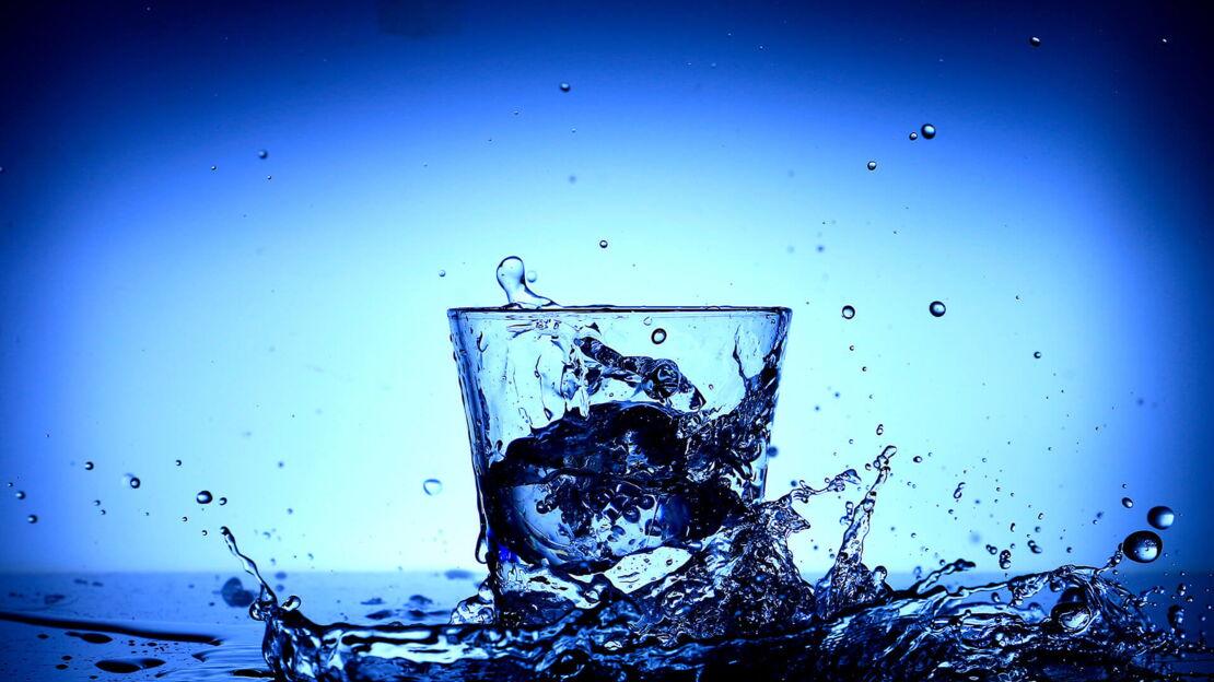 Spritzendes Wasser und ein Wasserglas vor blauem Hintergrund