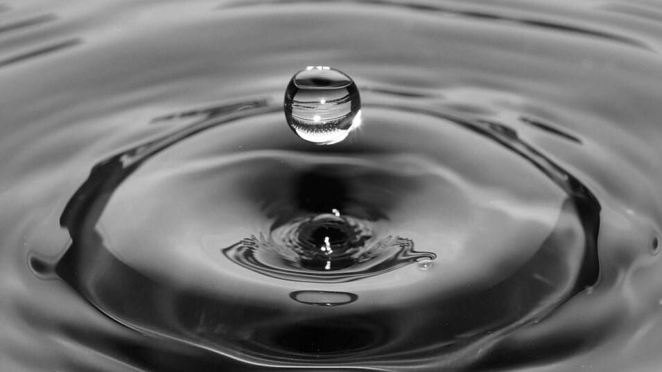 Wassertropfen auf Wasseroberflaeche in dunkler Optik