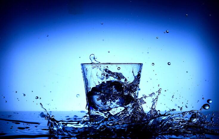 Spritzendes Wasser und ein Wasserglas vor blauem Hintergrund
