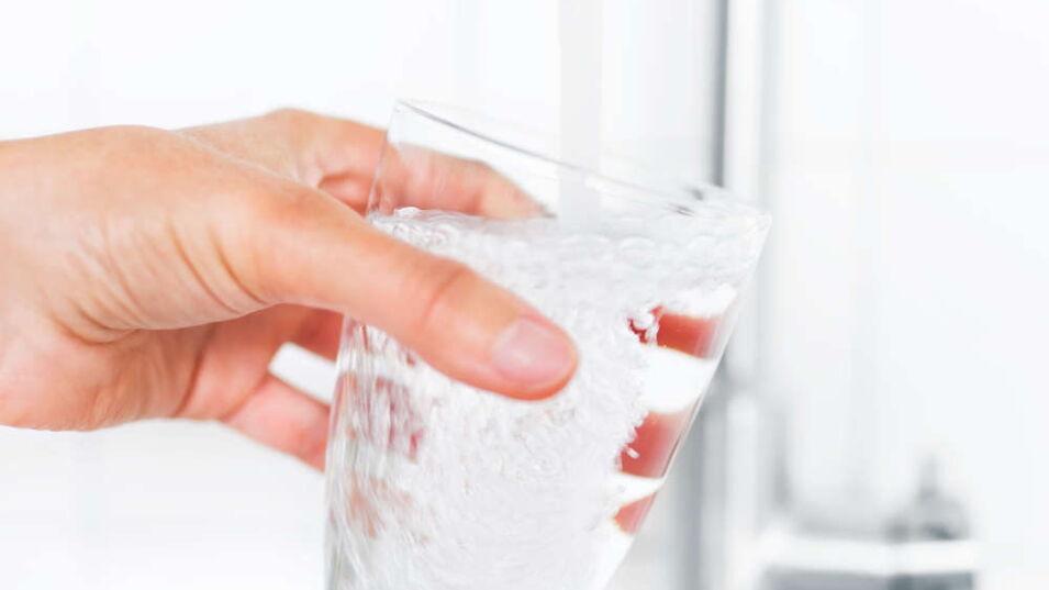 Ein Glas wird mit Wasser aus dem Wasserhahn gefüllt