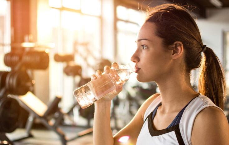 Sportliche junge Frau trinkt Wasser in einem Fittnesstudio