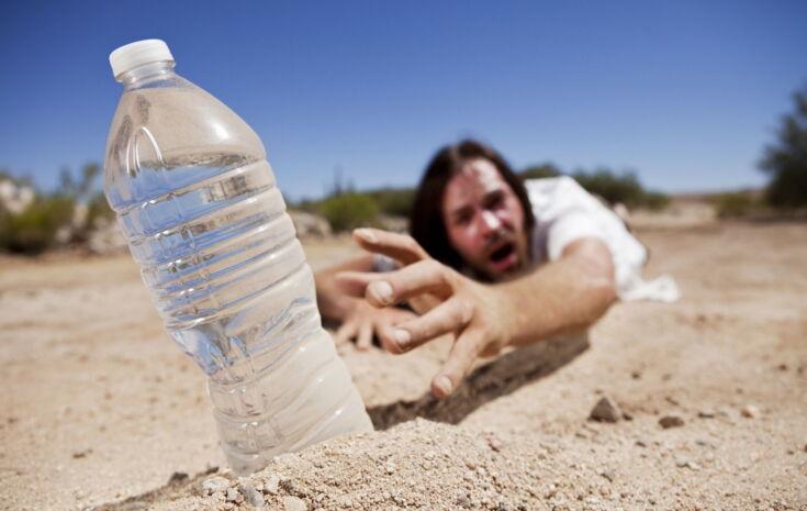 Mann greift nach Wasserflasche im Sand