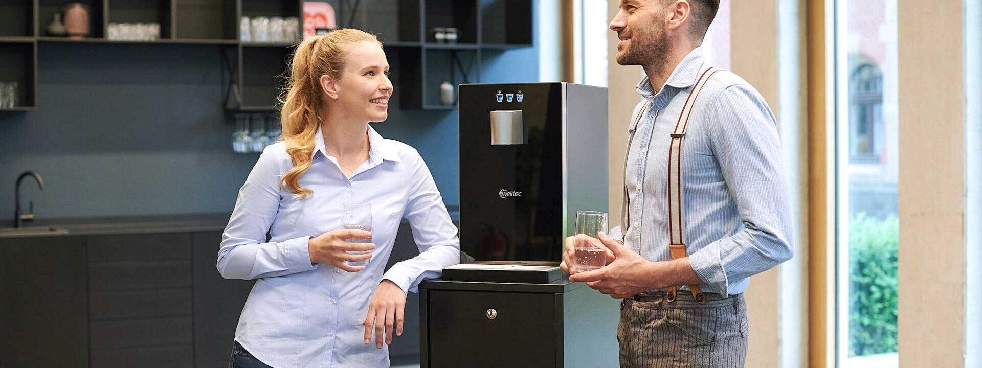 zwei Kollegen stehen am Cube Compact mit Unterschrank und trinken Wasser