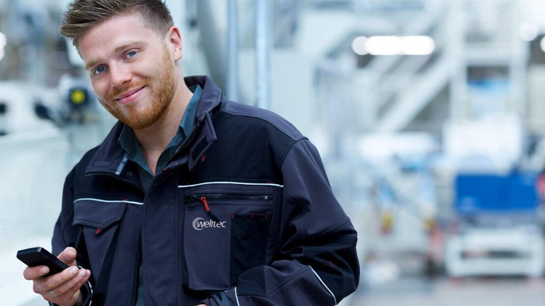 Junger Mann steht in Fabrik mit einem Handy in der Hand