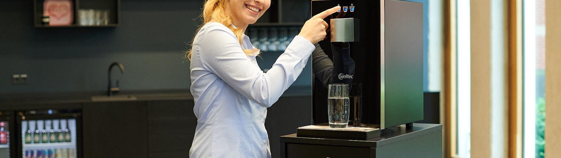 Junge Frau zieht sich ein Glas Wasser aus dem Wasserspender