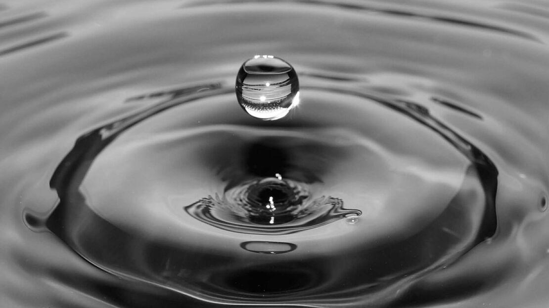 Wassertropfen auf Wasseroberflaeche in dunkler Optik