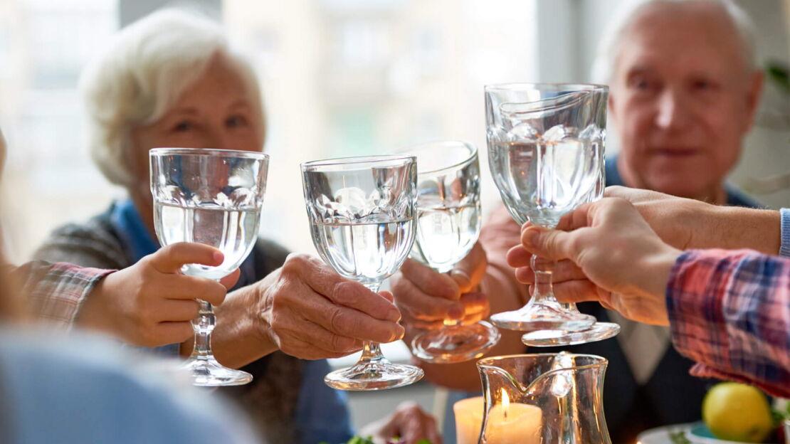 Eine Familie sitzt am Tisch und stößt mit Wasser an