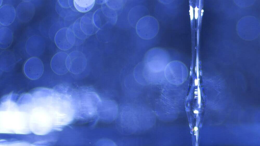 Wasserstrahl fließt in blaue Fluessigkeit