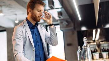 Mann trinkt aus Wasserglas und liest Zeitung