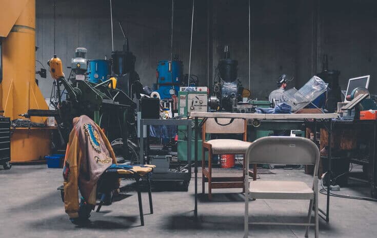 Fabrikhalle mit Tisch, Stuehlen und Maschinen im Hintergrund