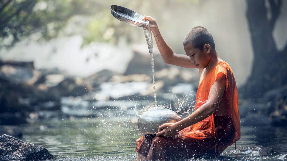 Ein Junge sitzt in einem Fluss und gießt Wasser auf einen Topf