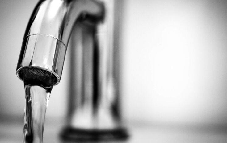Schwarz-Weiss-Fotografie eines Edelstahlwasserhahns mit Wasserstrahl