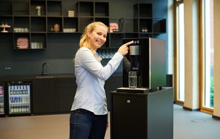 Junge Frau zieht sich ein Glas Wasser aus dem Wasserspender